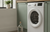 Glazen fles witte azijn naast een witte wasmachine in een lichte Nederlandse wasruimte